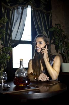 woman sits at the table and speaks by mobile phone in vintage restaurant