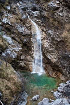 Waterfall falls into the green stream between rocks