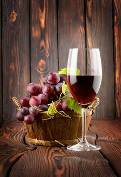 Wine glass and grapes in a basket on a wooden background