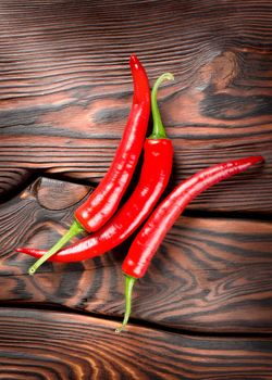 Three red chili peppers on a wooden background