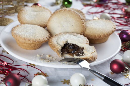 Mince pies on a plate surrounded by holiday decorations.