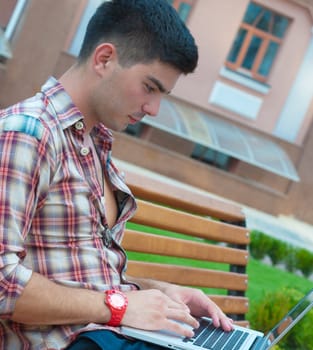 Young man sitting on a bench with a laptop on her lap.