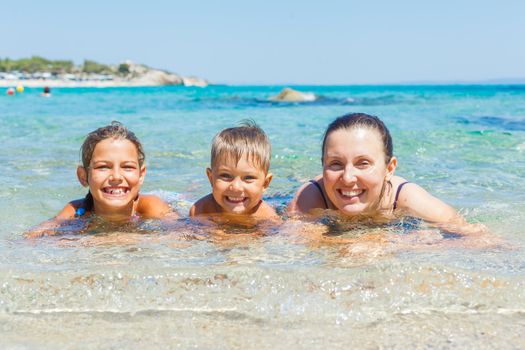 Family summer vacation - mother with her kids have fun and swimming in the transparent sea