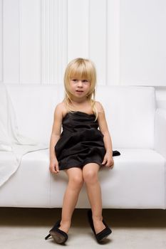 Girl 3 years old in her mother's high heels sitting on a white sofa