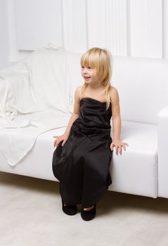 Girl 3 years old in her mother's high heels sitting on a white sofa