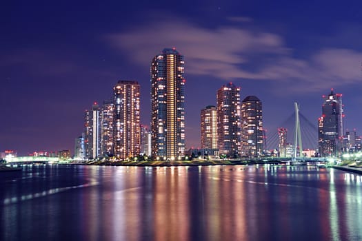 Tokyo skyline by night in modern Tsukishima district with scenic water reflection in Sumida river waters