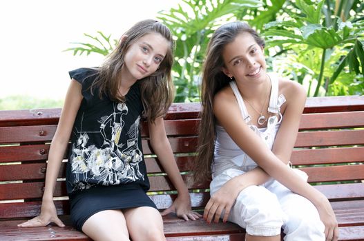 Portrait of two girls sitting on a bench in the park.
