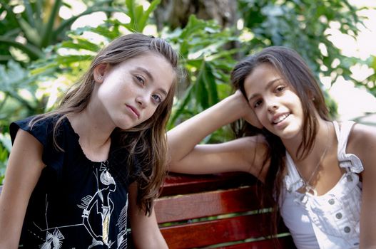 Portrait of two girls sitting on a bench in the park.