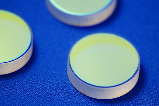 laser industry optical components on blue background; flat thick mirrors with special reflection coating used in Laboratory Science and in Laser Manufacture, macro-image sharp focus is  on the front mirror