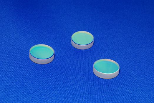  laser industry optical components ; flat thick mirrors with special reflection coating used in Laboratory Science and in Laser Manufacture on the blue canvas background