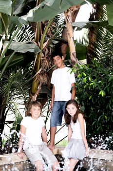 Portrait of three children near a fountain surrounded by tropical plants.