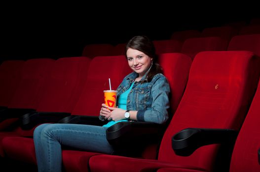 beautiful woman in a movie theater, watching a movie and drink a drink