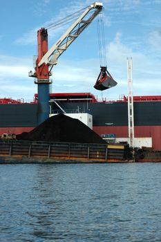coal is being loaded onto tankers with  crane from a pontoon