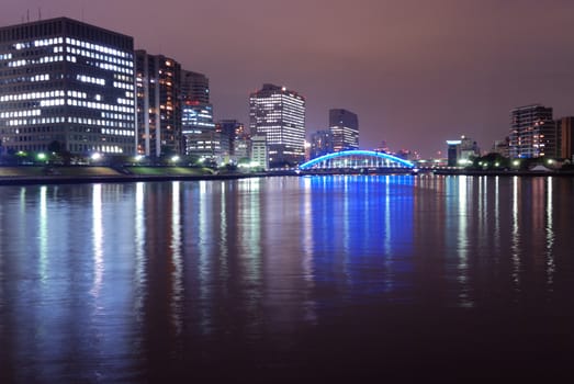  image of night Tokyo skyline  with scenic water reflection in Sumida river and metallic Eitai Bridge  illuminated by  blue