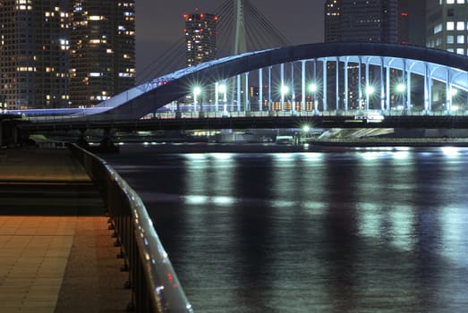 Sumida river embankment in central Tokyo by night with metallic Eitai bridge background