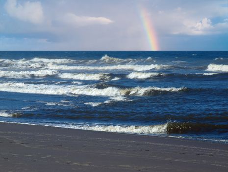 Ocean Waves Breaking on Shore with a Partial Rainbow in the Background