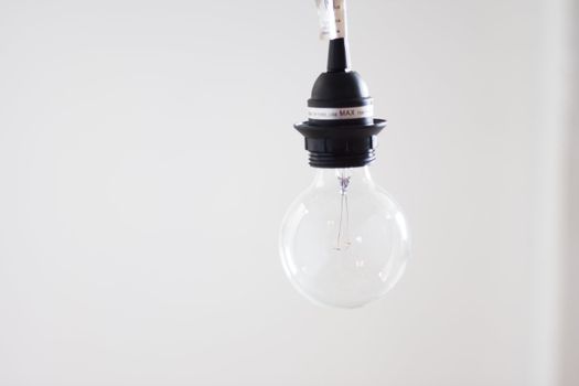 Clear hanging lightbulb against bright white background