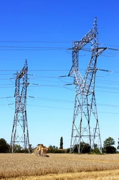 electric pylon on a field with a combine in a field of wheat