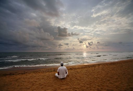 Guy meditating at sunset sitting on coastline 