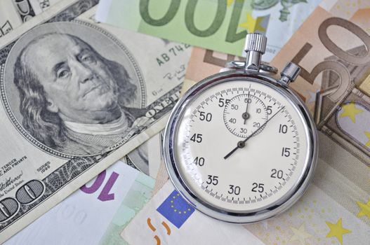 stopwatch lay over Euro and US dollar banknotes; focus on watch