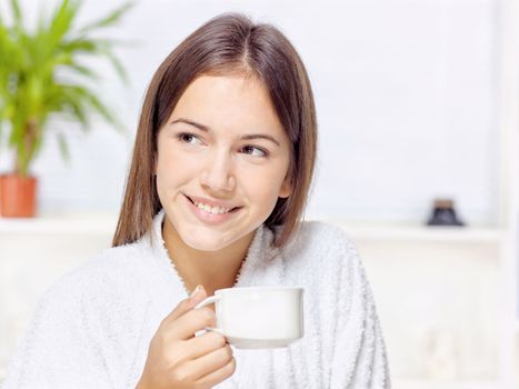 Woman in bathrobe holding cup at home