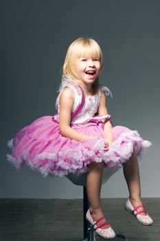 Portrait of a sweet infant wearing a pink tutu, necklace, and headband bow,  in studio sitting in a wicker child's chair