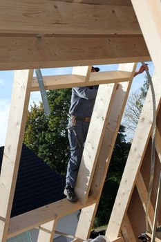 Carpenter working high up standing on a beam of wooden roof at construction site