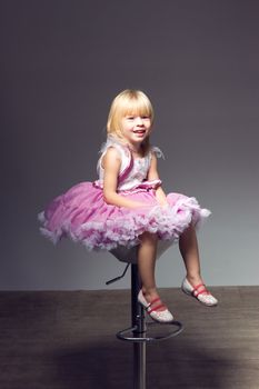 Portrait of a sweet infant wearing a pink tutu, necklace, and headband bow,  in studio sitting in a wicker child's chair