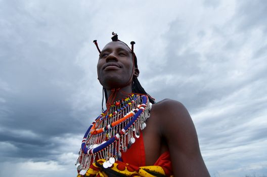 Village Masai Mara, Kenya – October  17, 2011: young Masai warrior is seen in his ceremonial dress. He is meeting visitors to his village where he demonstrates traditional culture. He is in the Masai Mara region of southwestern Kenya.