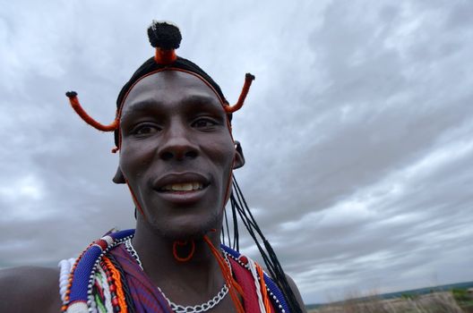 Village Masai Mara, Kenya – October  17, 2011: young Masai warrior is seen in his ceremonial dress. He is meeting visitors to his village where he demonstrates traditional culture. He is in the Masai Mara region of southwestern Kenya.