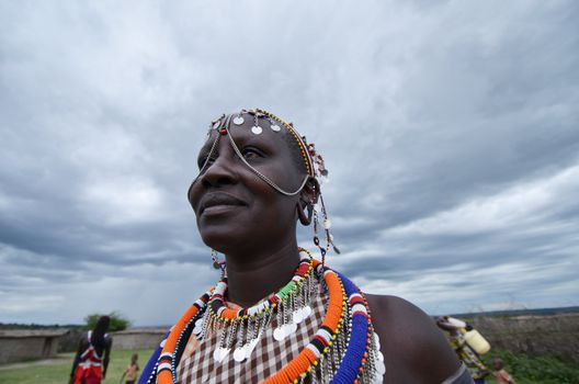 Village  Masai Mara, Kenya – October  17, 2011: Masai woman is seen in his ceremonial dress. He is meeting visitors to his village where he demonstrates traditional culture. She is located in the southwestern region of the Masai Mara in Kenya.