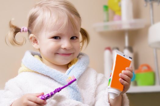 Smiling girl with toothbrush and tube in bathroom