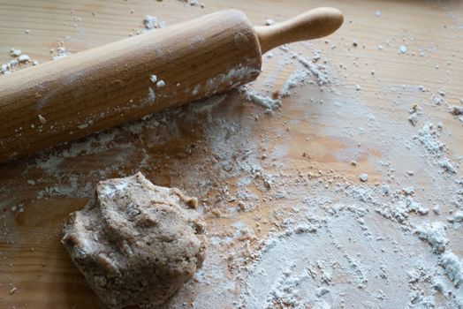 rolling pin with dough and flour on wooden board