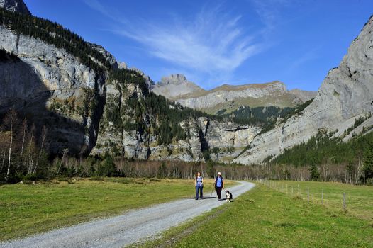 Two women and their dog walking in the alpine valley of Gasteretal, above Kandersteg, in Switzerland. Space for text in the sky.
