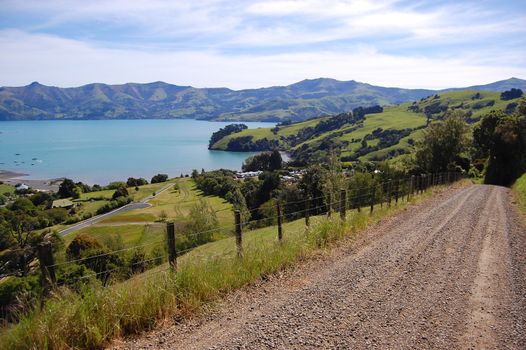 Rural gravel road with fence at farmland, sea bay view, Banks Peninsula, New Zealand