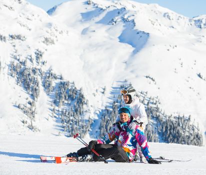 Happy man and his daughter sitting on top of Alps, resting after skiing against wonderful winter mountains background