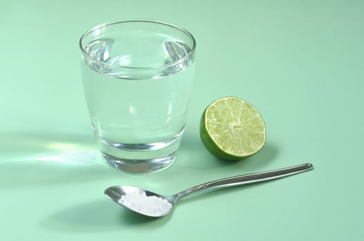 Glass of water with half lim and spoonful of salt on green table