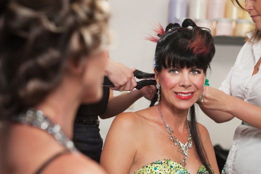 Smiling woman looking at lady with hair stylists working