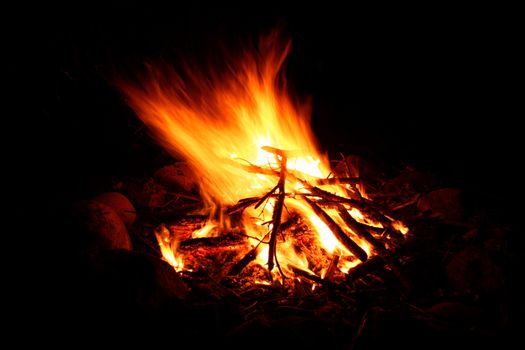 Flames of a cozy campfire flicker in a light breeze against a dark night.
