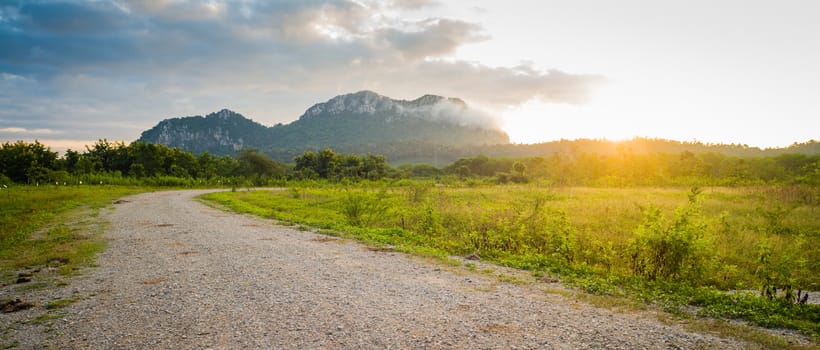 Field and dirt road to sunset behind mountain