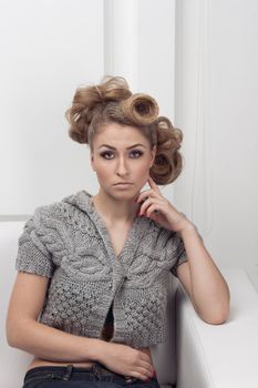 young, beautiful slim blonde girl in a gray jacket lying on a white sofa in a white studio