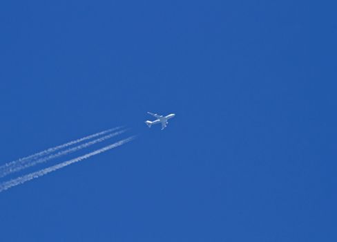 Jet passenger aircraft/plane flying high with vapour/vapor or contrails against blue sky