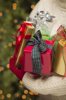 Woman Wearing A Sweater and Seasonal Red Mittens Against an Abstract Green and Golden Background Holding Beautifully Wrapped Christmas Gifts.