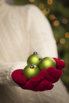 Woman Wearing A Sweater and Seasonal Red Mittens Holding Three Green Christmas Ornaments.