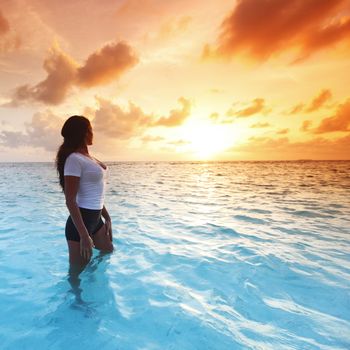 Beautiful woman in sea enjoying colorful sunset