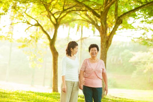 Asian senior mother and adult daughter walking at outdoor green park