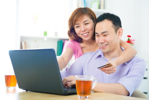 Happy Asian couple shopping online with credit card and computer at home