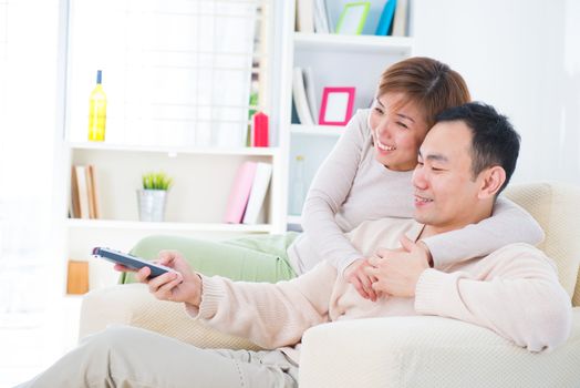 Portrait of happy Asian couple sitting on couch and watching television together