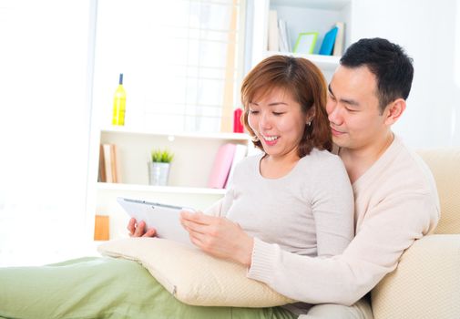 Beautiful Asian couple with digital tablet computer. Sitting on couch.