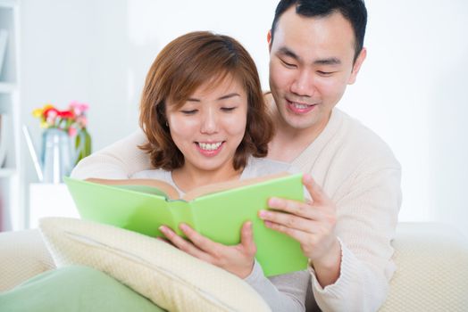 Beautiful loving Asian couple reading a book on the sofa